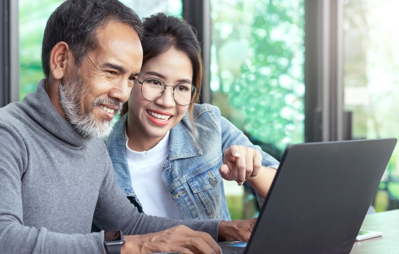 Smiling man and woman reviewing AARP-endorsed dental plans together on a laptop at home