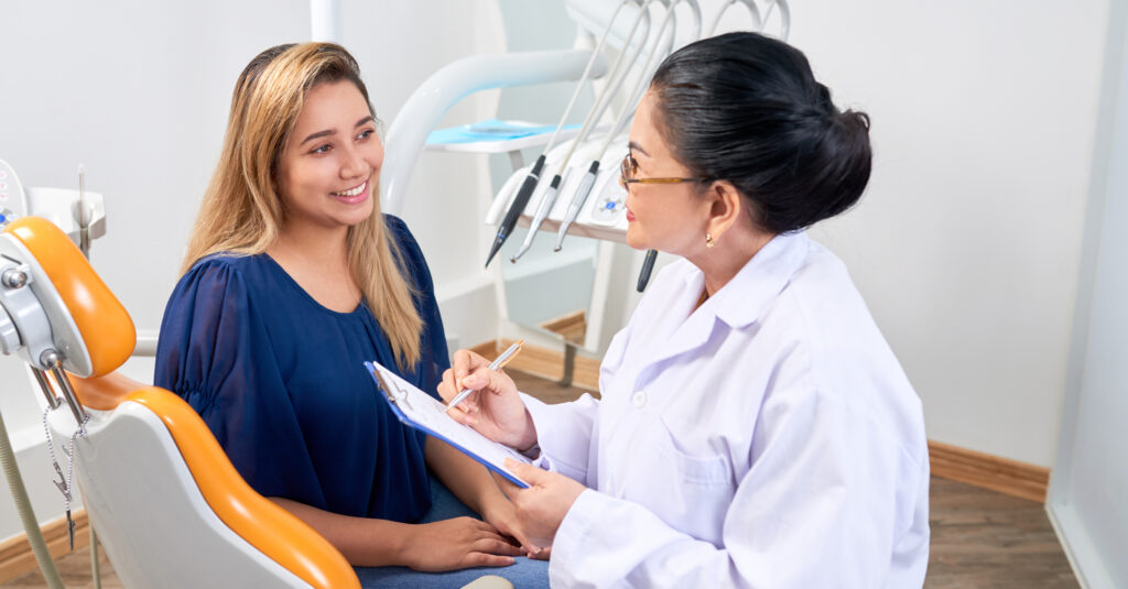 Pretty young woman talking to mature experienced dentist during annual check-up