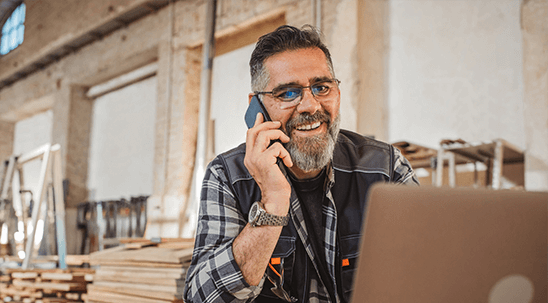 Small business owner in a workshop talking on the phone while working on a laptop